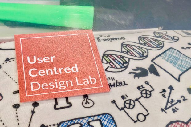 Coral coloured sticker saying "user centred design lab" on a clear plastic stationery box