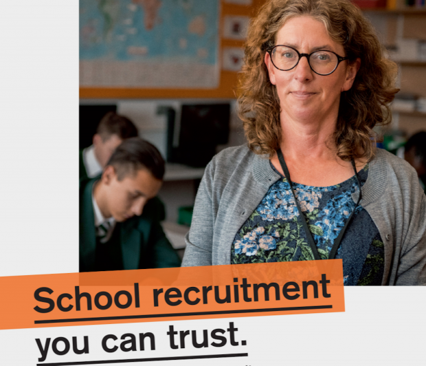 Teaching Vacancy service poster showing a woman teacher standing looking at the camera with pupils in uniform studying behind her