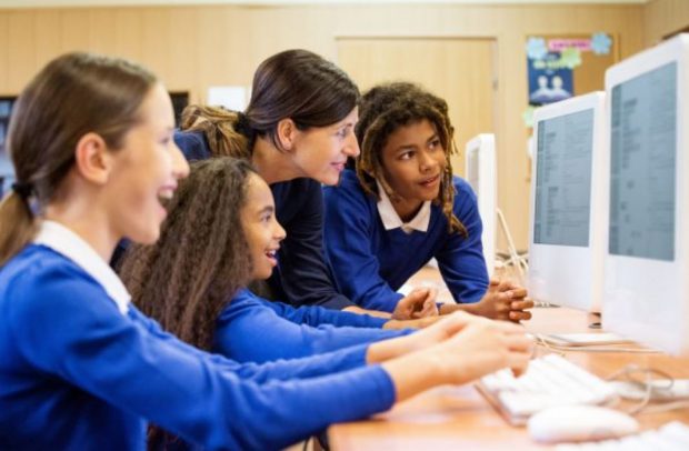 Three girl pupils from key stage 3 or 4 looking at a screen with their teacher