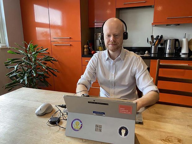 A man sitting at his laptop in his kitchen being interviewed.