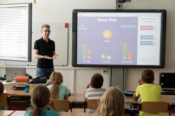 Male teacher with a classroom full of students looking at an interactive whiteboard 