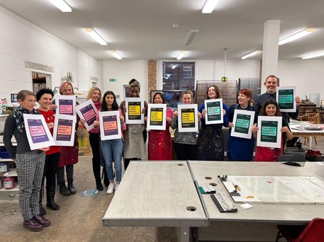 12 members of the design community holding up posters which they've created in a studio