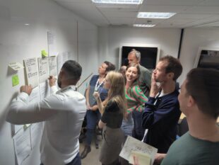 Half a dozen people gathered around a roadmap poster discussing and reviewing something